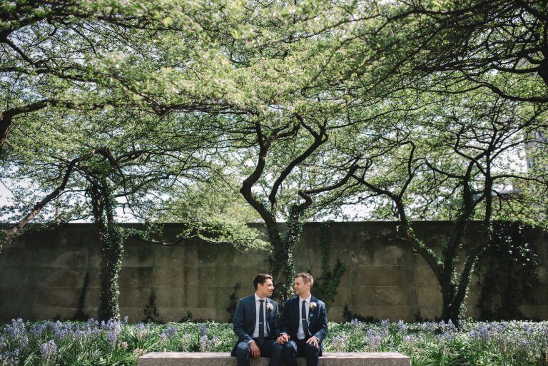 grooms in blue suits sit at art institute garden bench