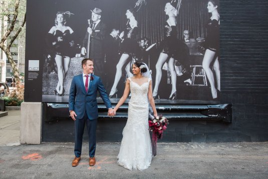 groom in blue suit and bride in lace dress hold hands in front of chez mural