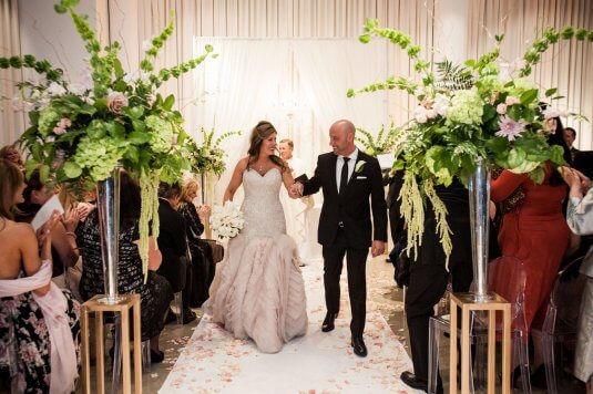 bride in blush beaded dress and groom walk down floral covered ceremony