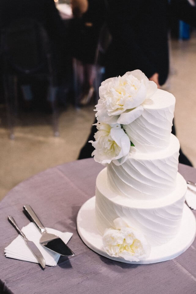white 3 layer cake topped with white peonies on purple table