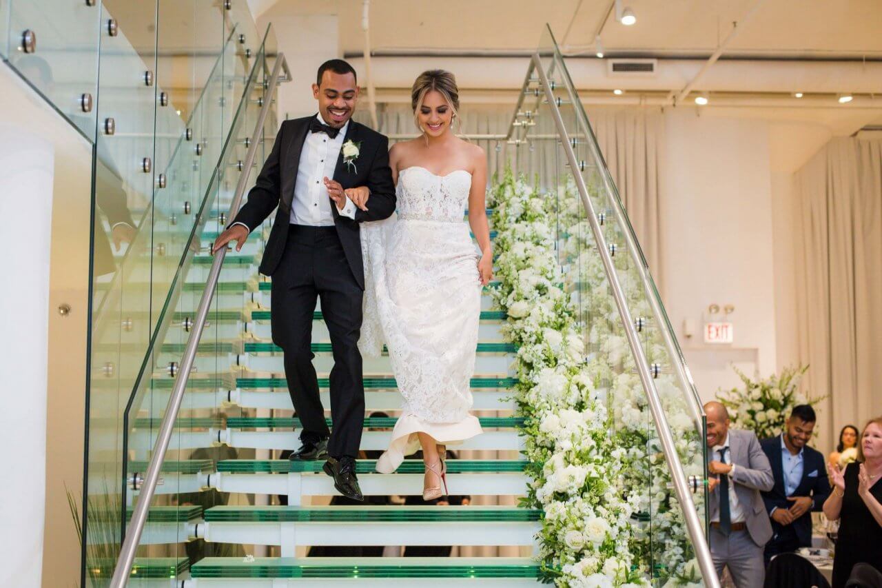 chicago newlyweds walking down glass staircase lined with modern wedding floral at chez wedding venue