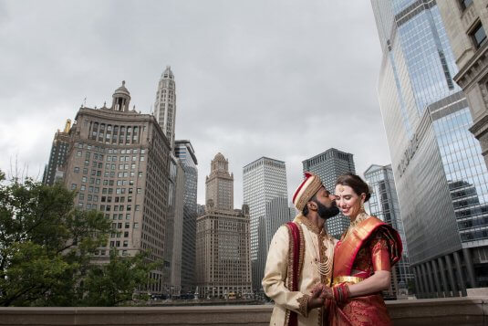 bride in groom in traditonal red and gold indian wedding clothing by the chicago river