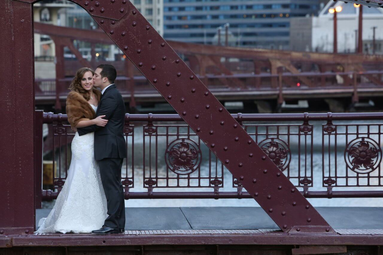 groom kisses bride on cheek on chicago river bridge