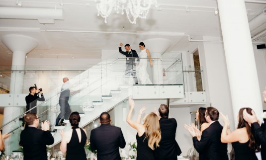 chicago bride and groom joanna and corey make grand entrance on glass staircase for modern white wedding at chez chicago wedding venue