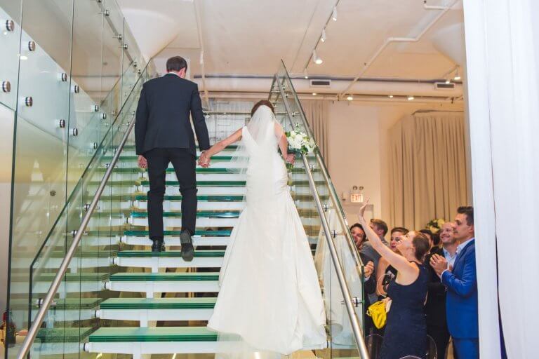 bride and groom hold hands and walk up chez glass staircase