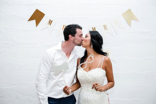 bride and groom kiss in front of white brick wall with props