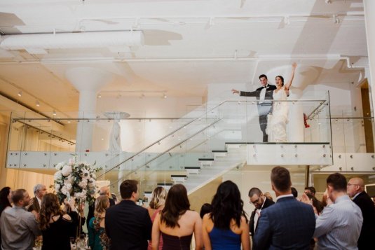 bride and groom throw hands up at the top of the chez glass staircase in excitment