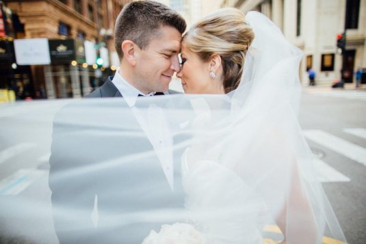 bride and groom smile and the brides veil blows in the wind