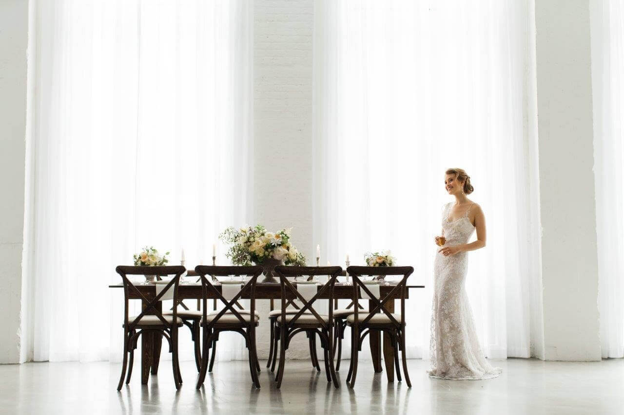 brid ein white lace dress standing by wooden table in white space