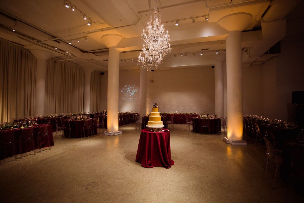 wedding reception setup burgundy tables and gold cake under chandeliers