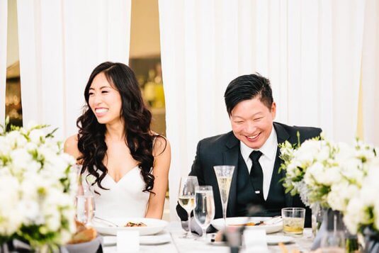 bride and groom smile and laugh at green and white weding reception