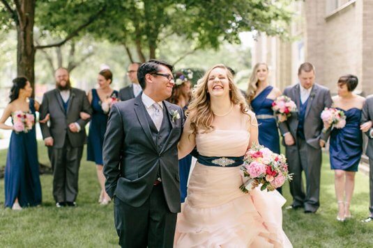 bride in pink dress and groom walk with bridal party in blue behind them