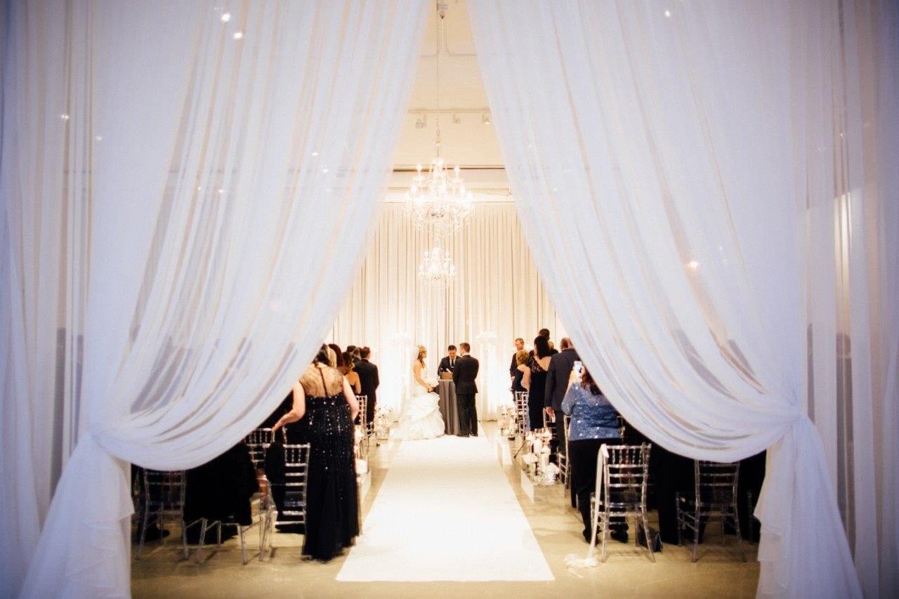swagged drape entrance to silver and white wedding ceremony with chandeliers