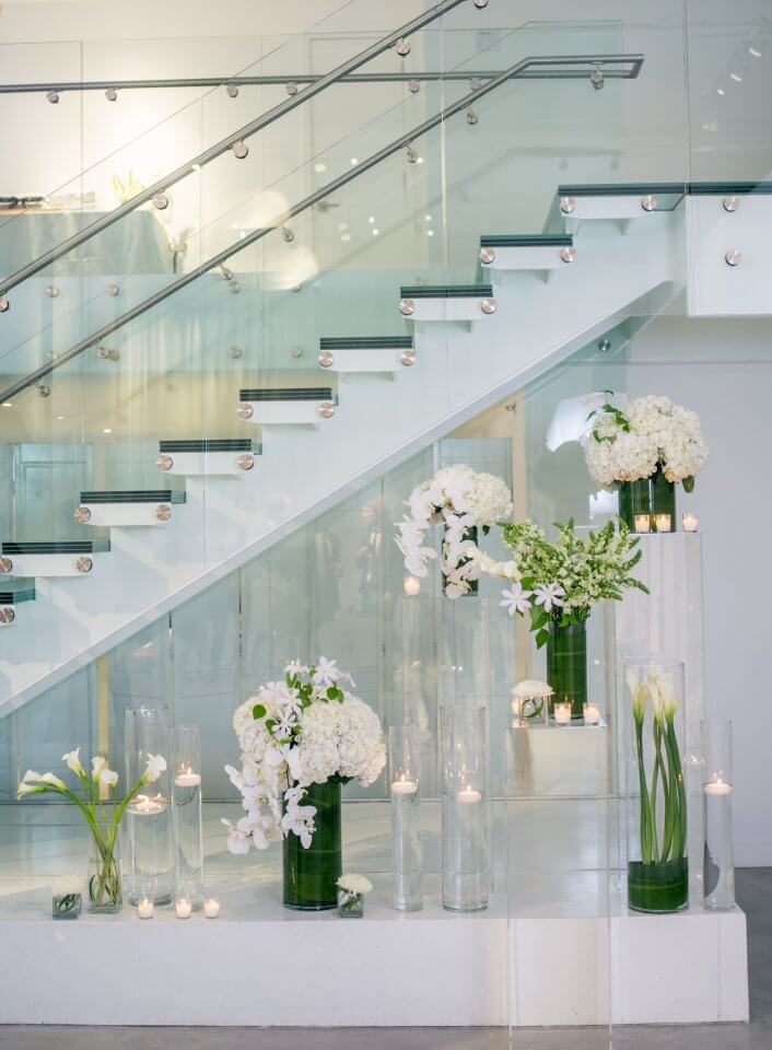 lucid stands and candles underneath chez staircase with white and green florals