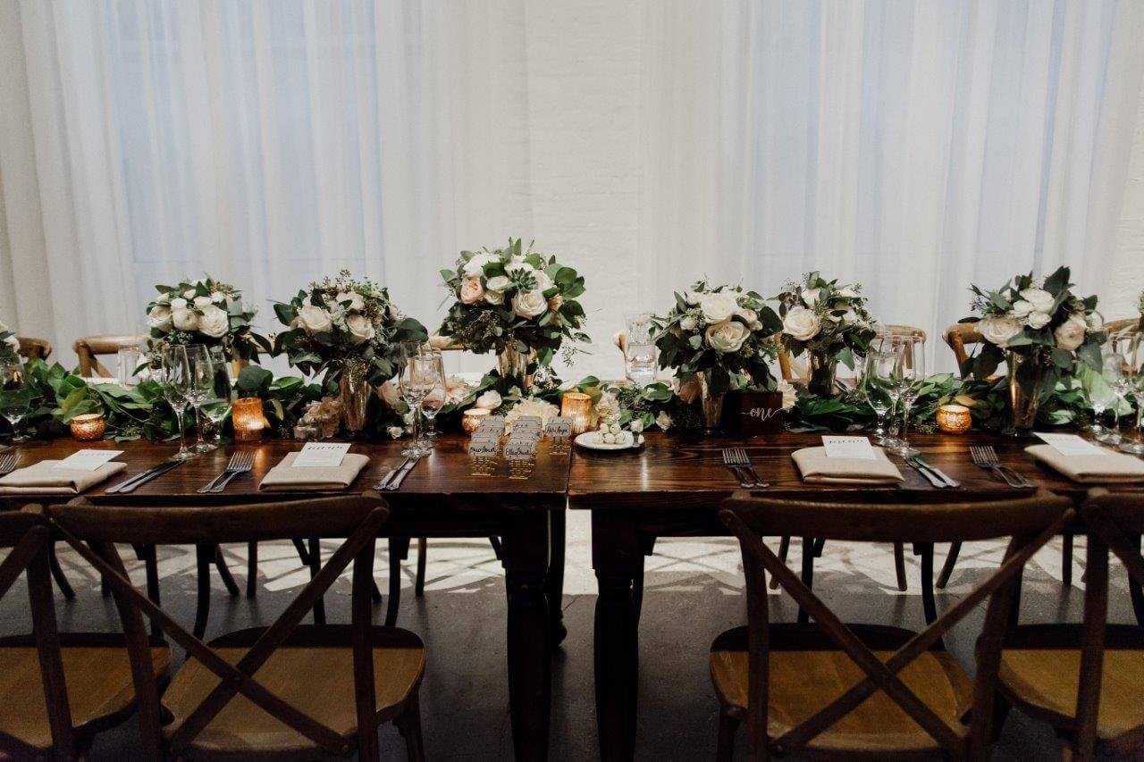 wooden wedding table with green and white floral centerpieces