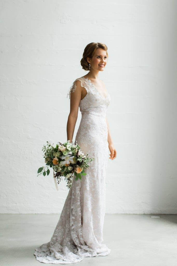 bride in white lace dress holding boquet of green white and peach florlas