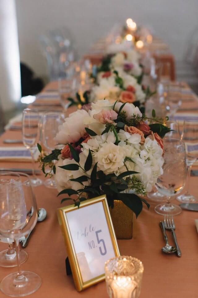 gold framed wedding table number in front of floral wedding centerpieces