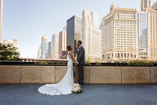 bride and groom hold hands by riverwalk