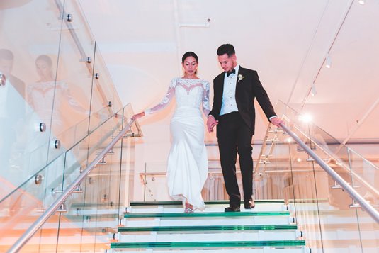 bride and groom walk down glass staircase