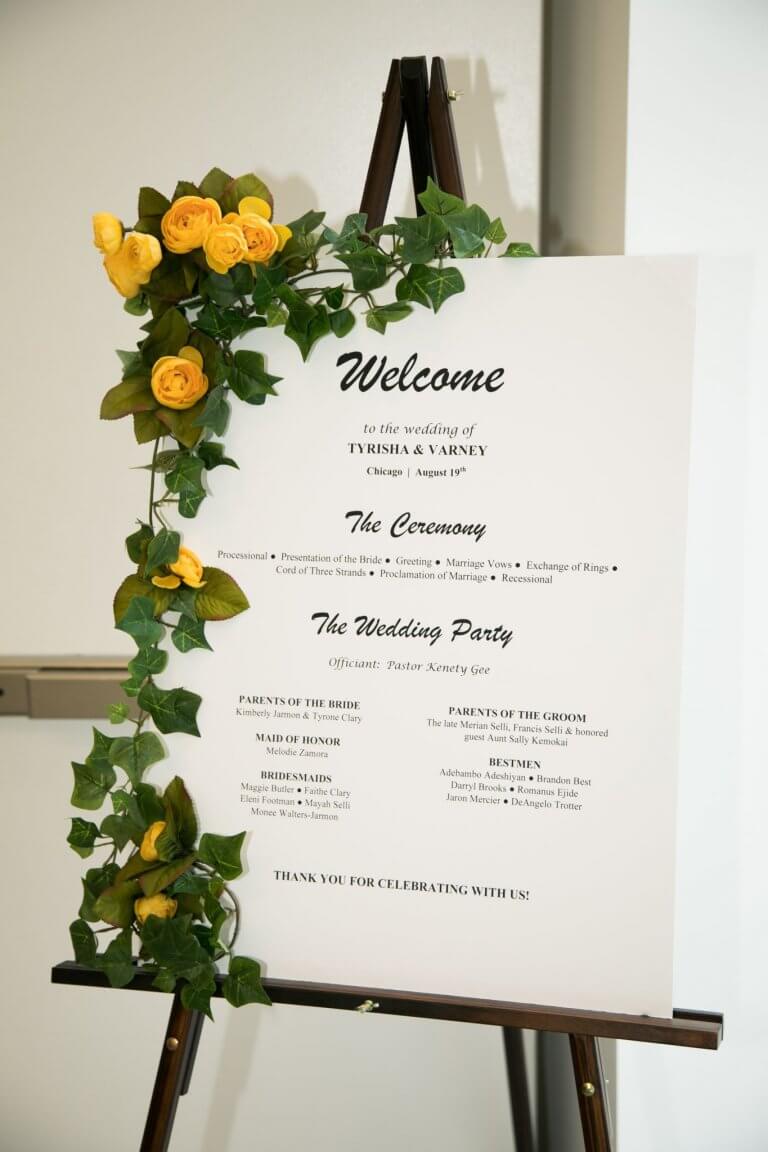 greenery and yellow roses line white welcome sign