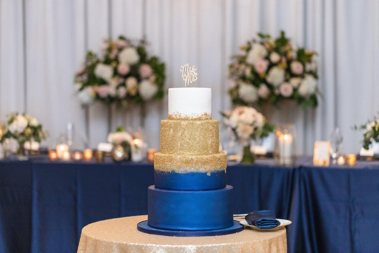 nacy and gold weding cake with cake topper on gold sequin table