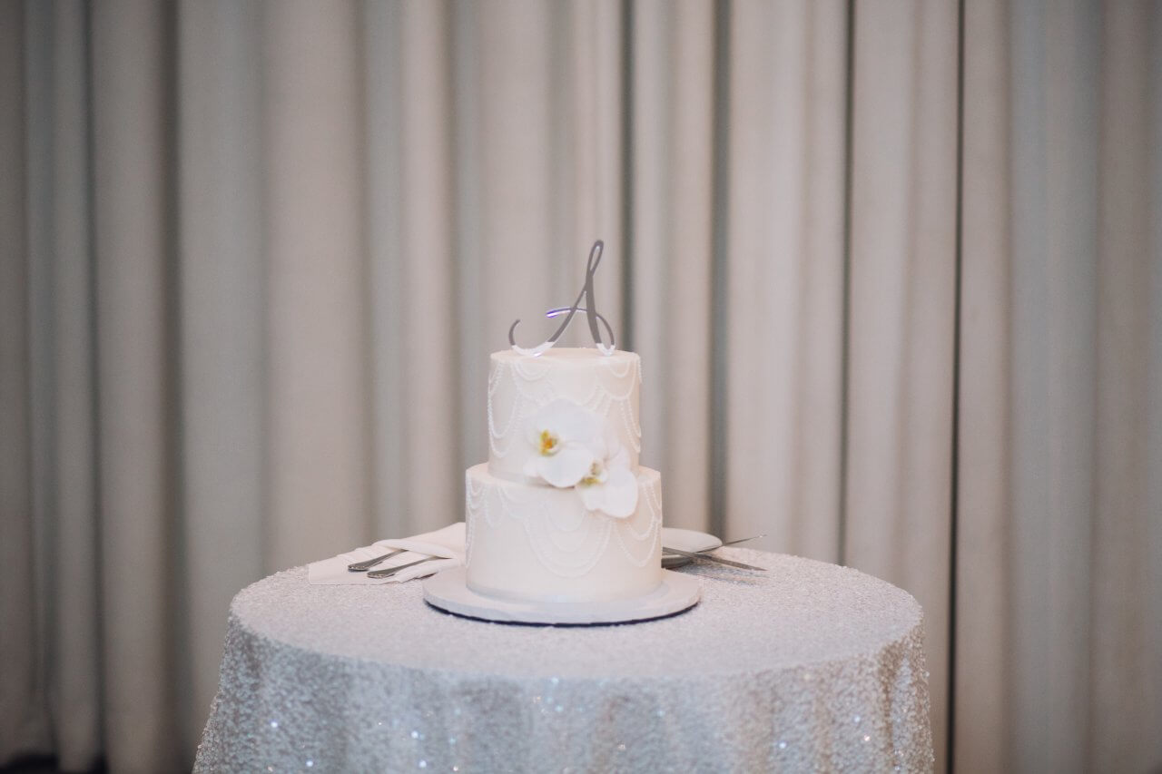 two layer white cake on white sequin table with silver cake topper