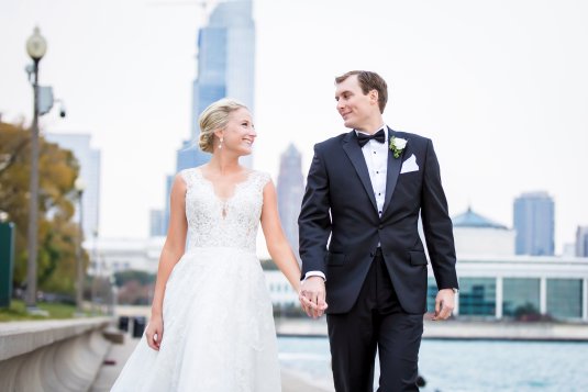 bride and groom hold hand on lakefront