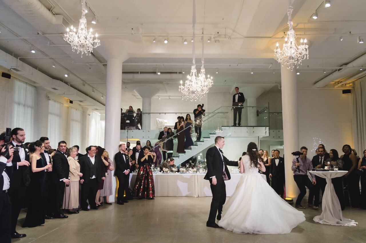 bride and groom dance under chandeliers in loft venue
